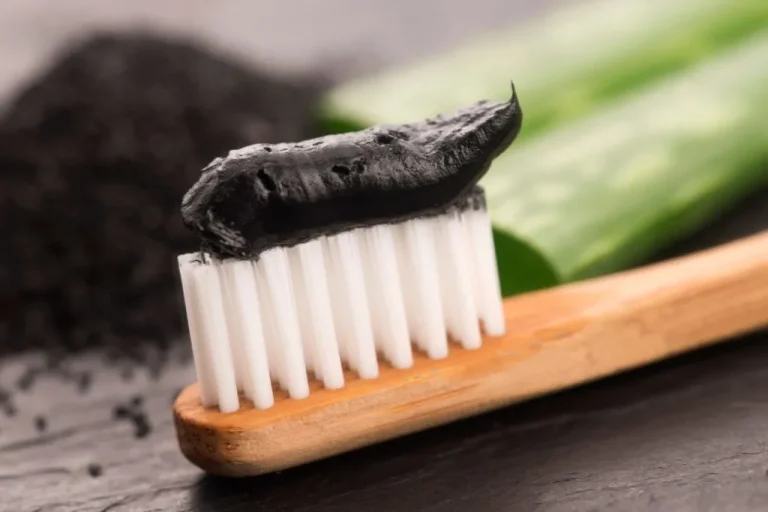 Black charcoal toothpaste on a bamboo toothbrush beside activated charcoal